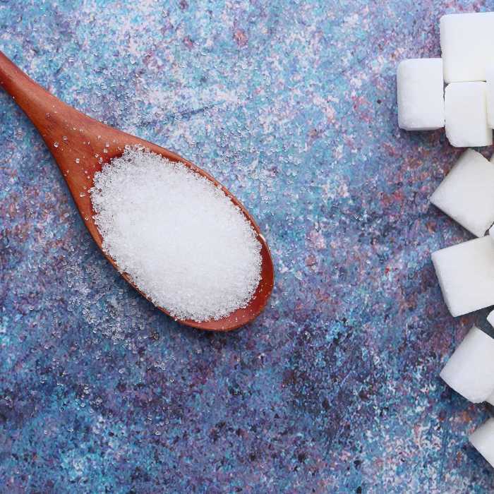 Wooden spoon with sugar and sugar cubes to the side of the spoon